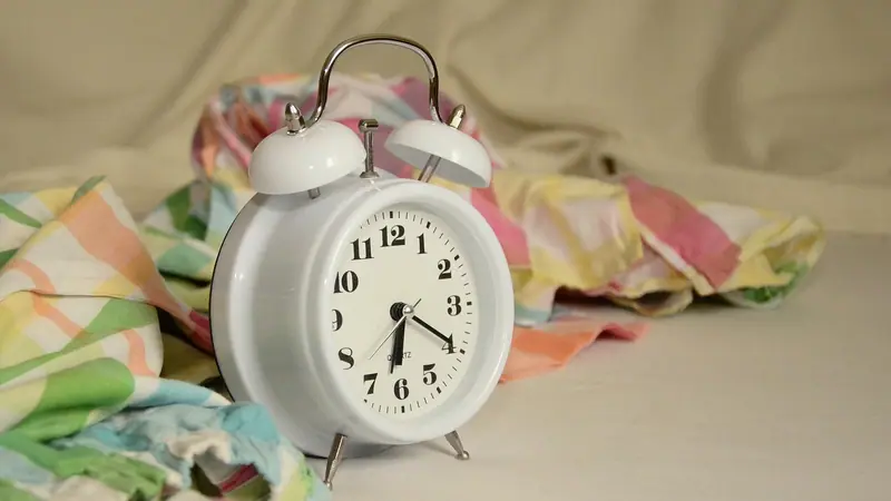 Despertador branco sobre a cama, entre lençóis coloridos amassados, na luz da manhã