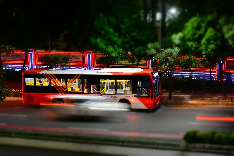 Ônibus vermelho passando em movimento por uma rua iluminada à noite