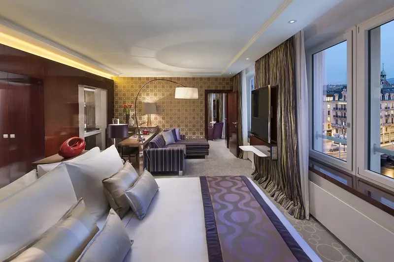 Quarto amplo e elegante com cama de casal, poltronas e janelas grandes com cortinas
