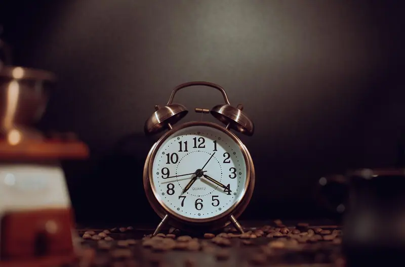 Despertador antigo de metal sobre uma mesa, num ambiente com pouca luz