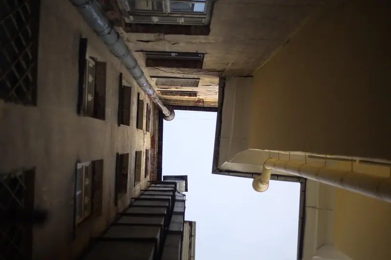 Vão estreito entre dois prédios visto de baixo, com janelas e um pedaço de céu