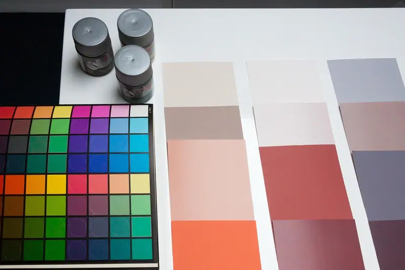 Cartela de cores, potes de tinta e amostras de pintura em tons claros sobre uma mesa branca