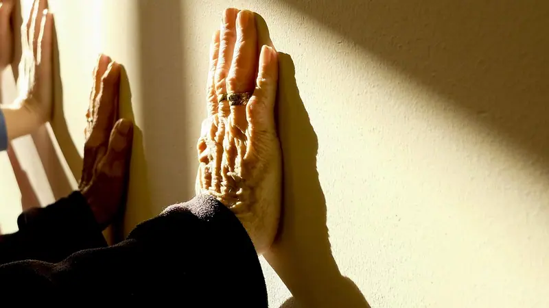 Mãos apoiadas numa parede clara, iluminada pelo sol
