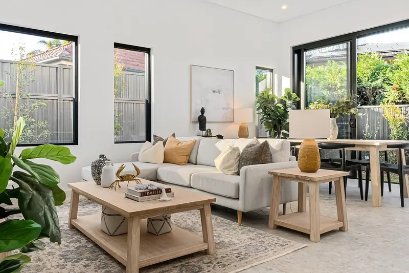 Sala de estar clara com sofá, mesa de centro de madeira, plantas e janelas amplas