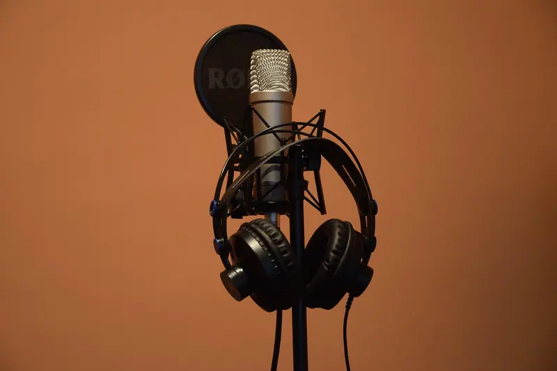 Microfone de estúdio com fone de ouvido pendurado no suporte, contra uma parede laranja