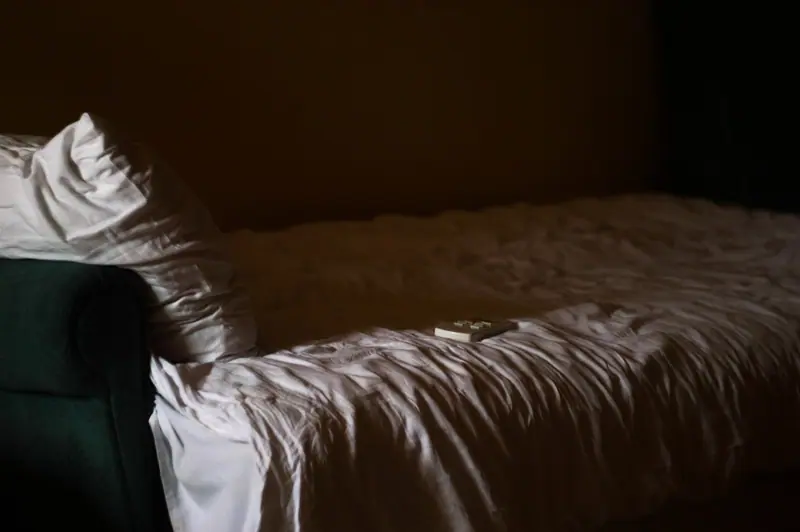 Cama desarrumada com lençóis amassados num quarto na penumbra