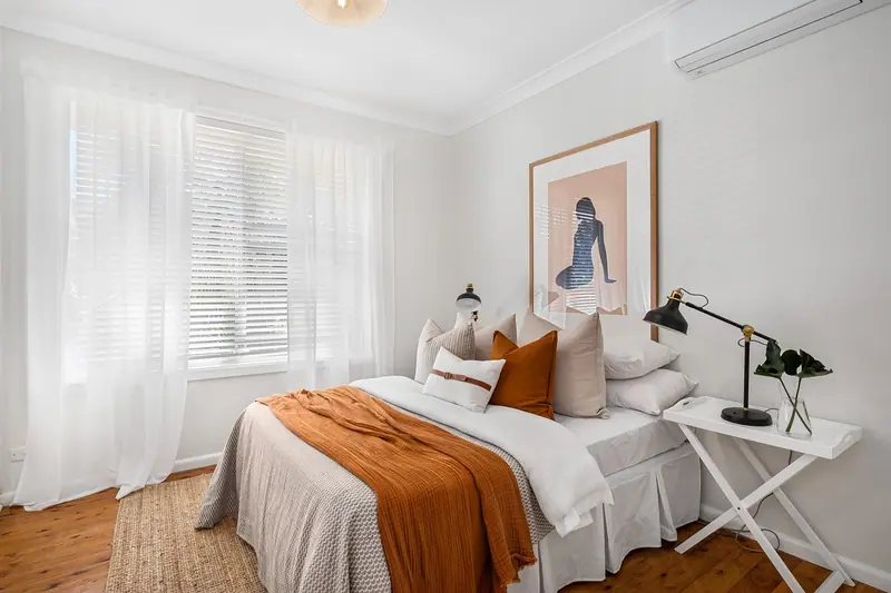 Quarto claro com cama arrumada, mesa de cabeceira e janela com persiana e cortina