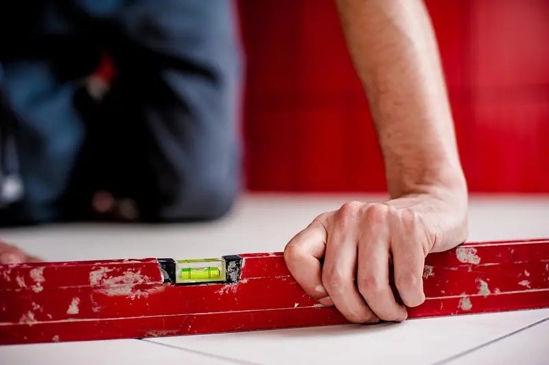 Mãos apoiando um nível de bolha vermelho sobre um piso de cerâmica branca
