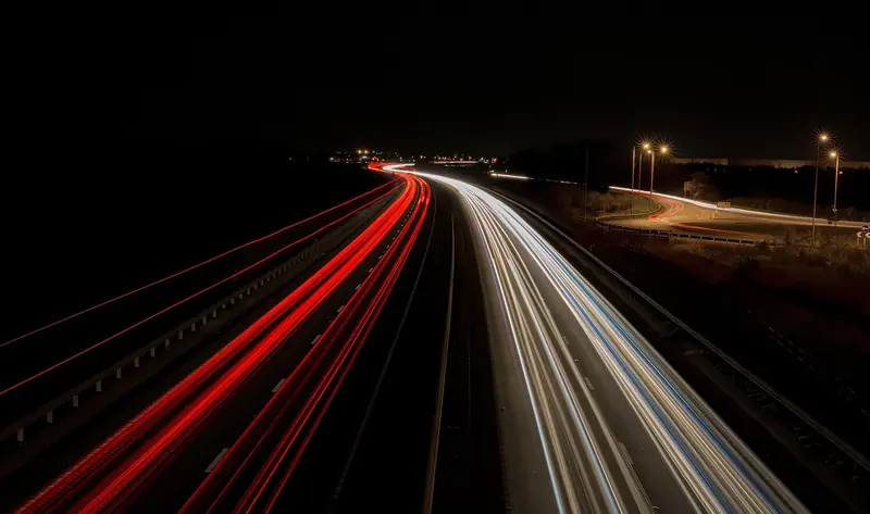 Rastros de luz vermelha e branca dos veículos numa via expressa à noite