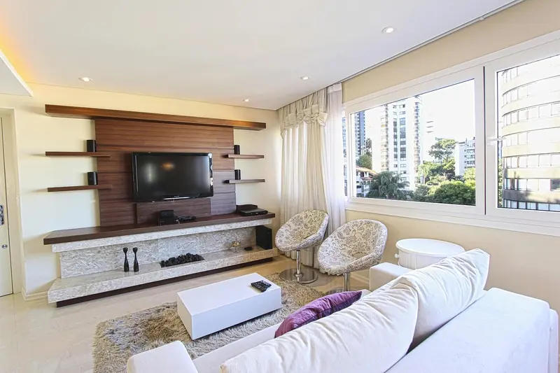 Sala de apartamento clara, com sofá branco e janelas amplas voltadas para prédios vizinhos