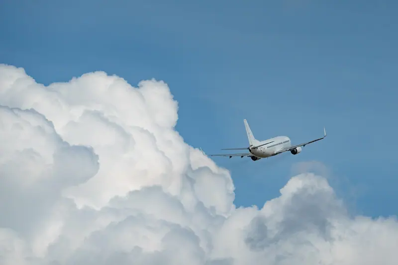 Avião de passageiros voando ao lado de nuvens altas num céu azul