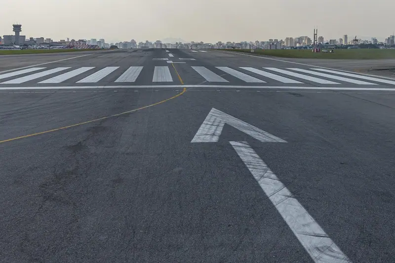 Pista de aeroporto vista do chão, com prédios da cidade no horizonte