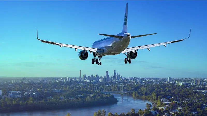 Avião com o trem de pouso baixado se aproximando, com a cidade e um rio ao fundo