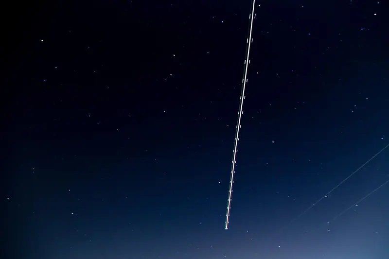 Rastro de luz de um avião atravessando o céu estrelado à noite
