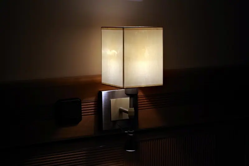 Abajur aceso ao lado da cabeceira de uma cama, em um quarto escuro