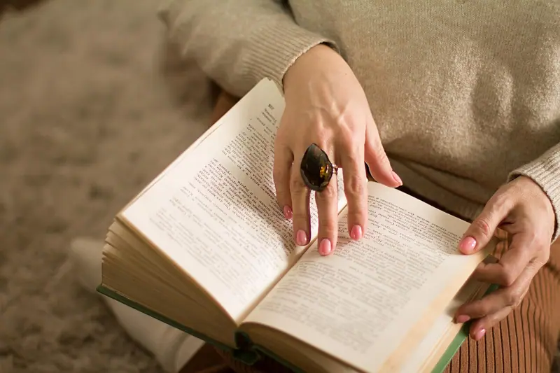 Mãos segurando um livro aberto no colo, sobre um tapete claro
