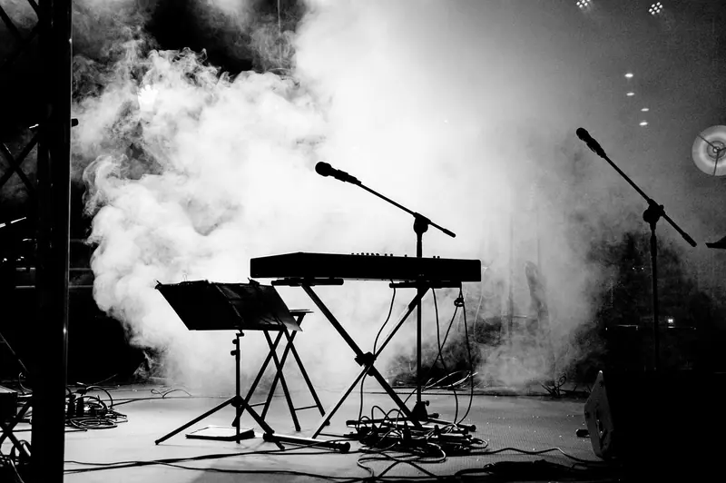Palco vazio em preto e branco, com teclado, pedestais de microfone e fumaça ao fundo