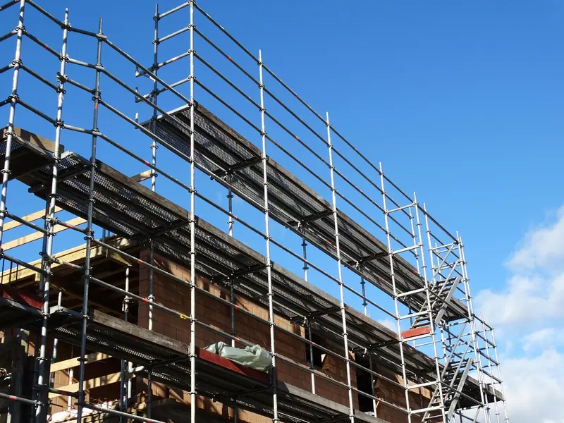 Andaimes metálicos montados na fachada de um prédio em construção, vistos de baixo contra o céu