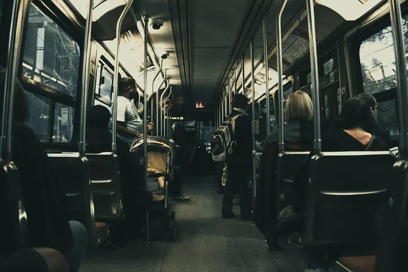 Interior de um ônibus à noite, com passageiros sentados de costas e luz fraca