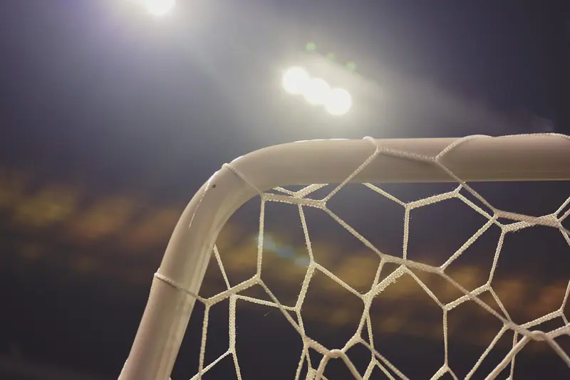 Canto de uma trave de futebol com a rede, iluminada por refletores acesos à noite