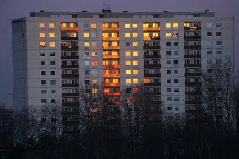 Prédio residencial alto ao entardecer, com várias janelas acesas e árvores na frente