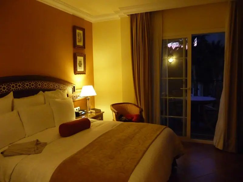 Quarto de casal à noite, com abajur aceso e porta de vidro fechada para a varanda