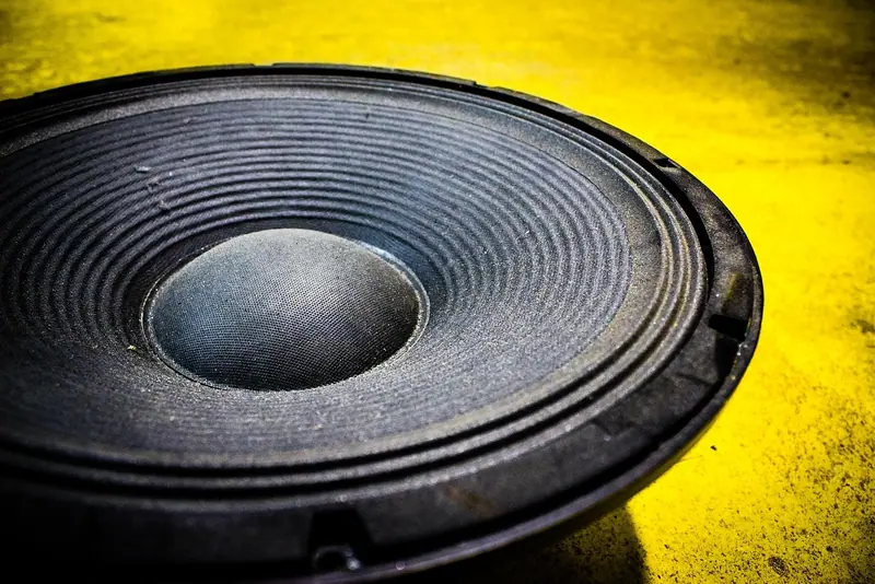 Close de um alto-falante de grave grande, com o cone escuro sobre um fundo amarelo