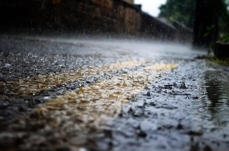Gotas de chuva batendo no asfalto molhado, em close, com a faixa amarela da pista desfocada
