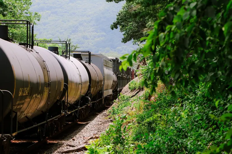 Fila de vagões-tanque de um trem de carga passando por uma ferrovia cercada de mata, num dia de sol