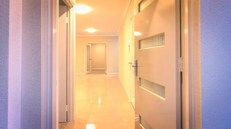 Corredor claro de prédio com piso brilhante e uma porta entreaberta em primeiro plano