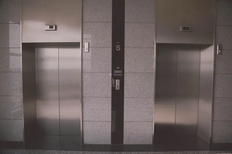 Duas portas de elevador de aço inox numa parede de granito