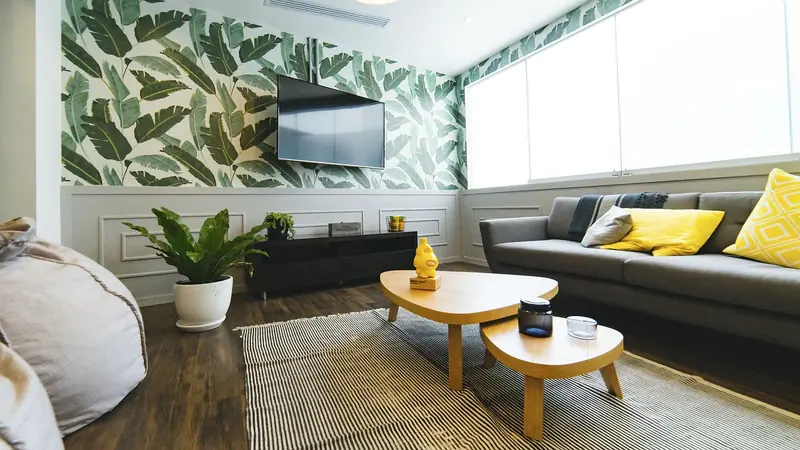 Sala com sofá cinza, mesinhas de madeira e um tapete listrado sobre o piso