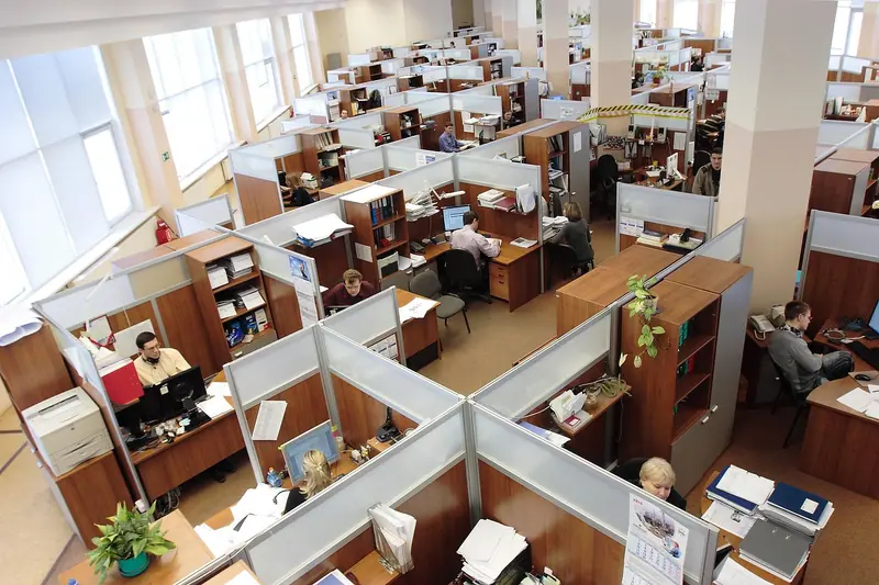 Escritório aberto visto de cima, com várias baias, computadores e pessoas trabalhando