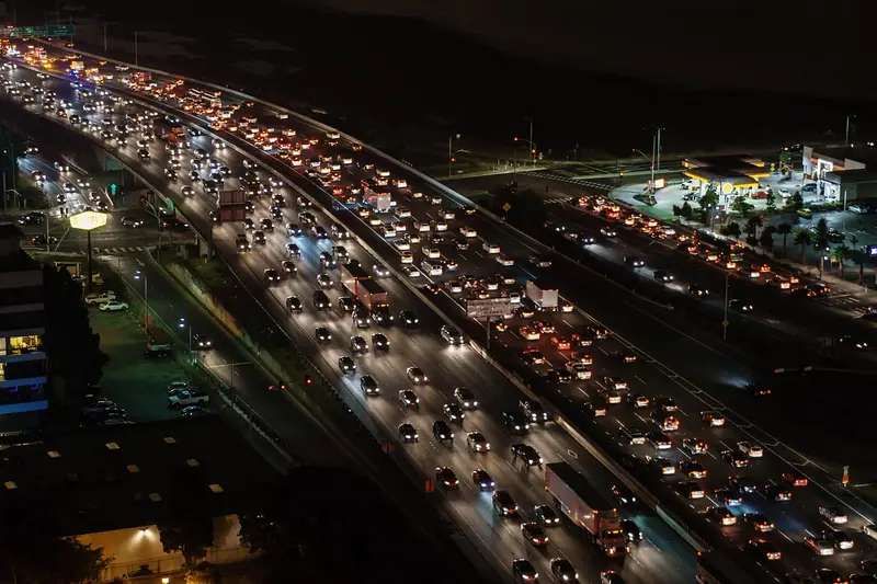 Avenida larga congestionada à noite, vista do alto, com faróis e luzes da cidade ao redor