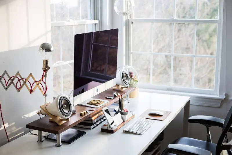 Mesa de trabalho com computador junto a uma janela clara, num escritório em casa