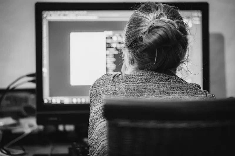 Mulher de costas trabalhando diante de um monitor, em foto preto e branco