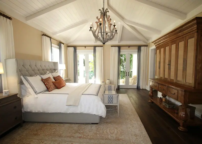 Quarto claro com cama de casal arrumada, cortinas abertas e portas envidraçadas ao fundo