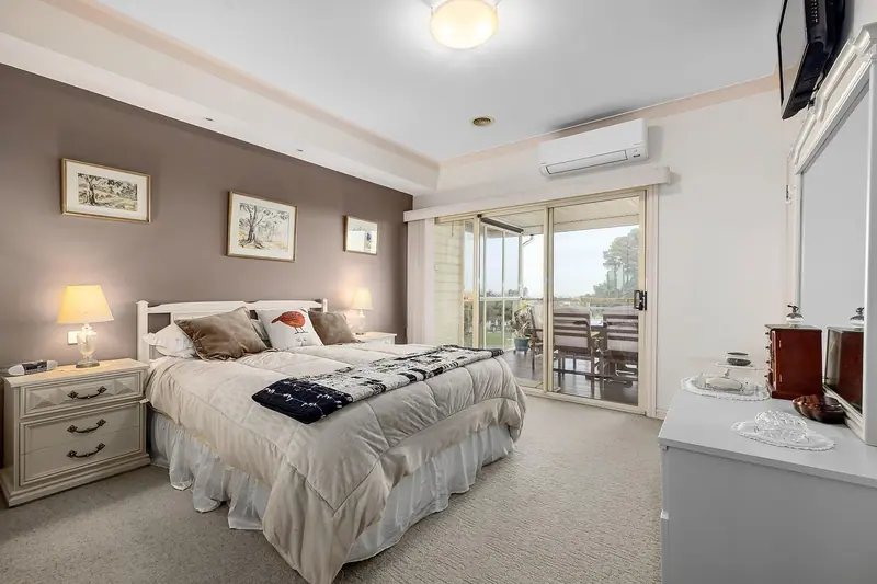 Quarto amplo com cama de casal arrumada, abajur aceso e porta de vidro para a varanda