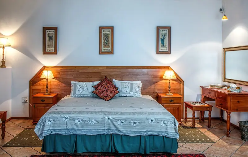 Quarto com cama de casal, cabeceira de madeira e dois abajures acesos sobre as mesas de cabeceira