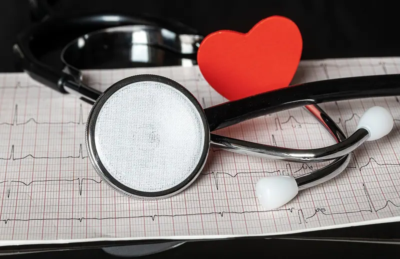 Estetoscópio sobre papel de eletrocardiograma, ao lado de um coração vermelho de papel