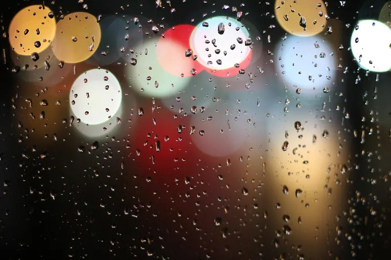 Gotas de chuva no vidro de uma janela, com as luzes da cidade desfocadas ao fundo, à noite