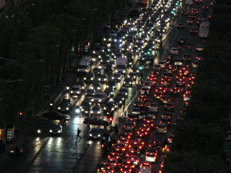 Avenida congestionada vista do alto à noite, com faróis brancos de um lado e lanternas vermelhas do outro