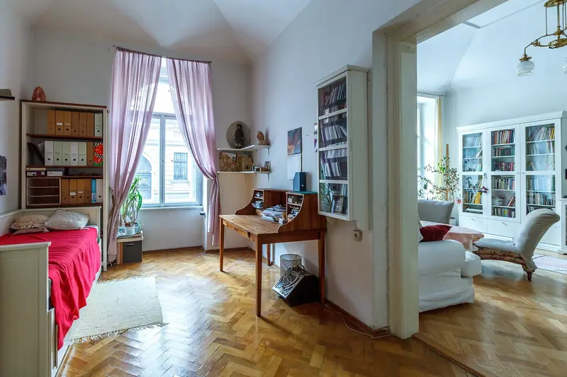 Apartamento antigo com piso de madeira em espinha de peixe, estantes e janelas altas com cortinas
