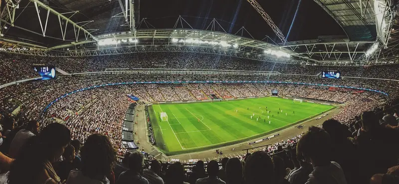 Estádio de futebol lotado à noite, com refletores acesos e o gramado iluminado