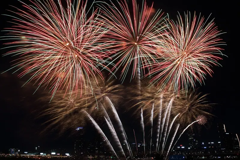Fogos de artifício dourados e rosados estourando no céu escuro, sobre as luzes da cidade