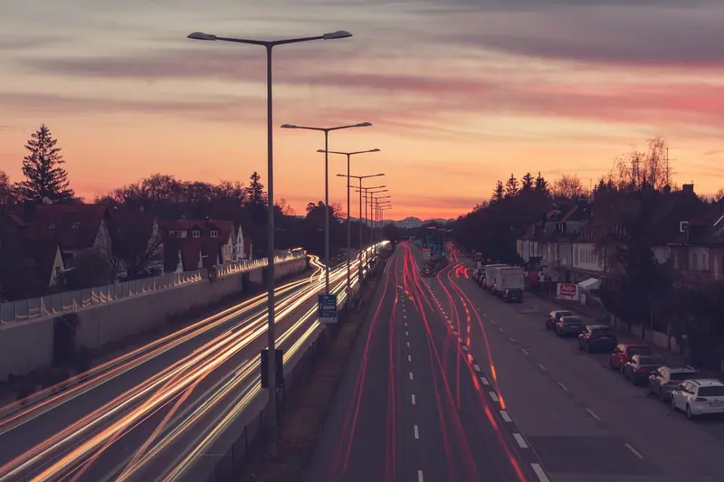Avenida ao entardecer com rastros de luz dos carros e postes acesos dos dois lados
