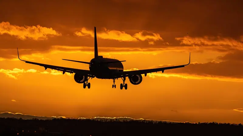 Avião de passageiros descendo ao entardecer, com o céu alaranjado e as luzes da cidade lá embaixo