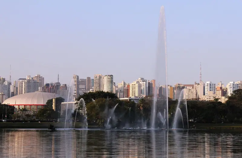 Lago com chafariz no Parque Ibirapuera, com árvores e prédios altos ao fundo