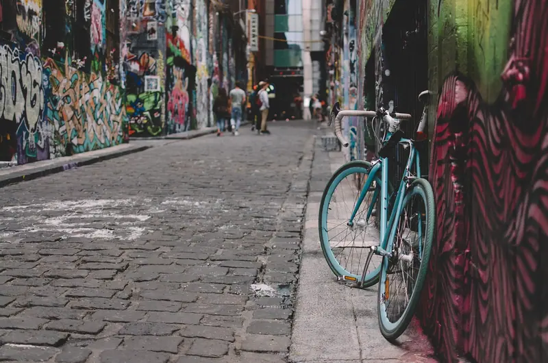 Beco de pedras com paredes cobertas de grafites coloridos e uma bicicleta encostada