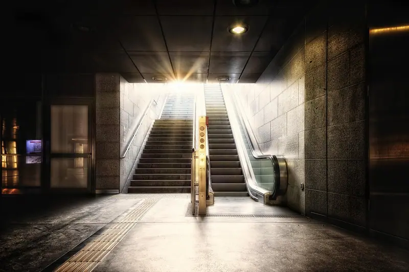 Escada fixa e escada rolante de uma estação subterrânea levando à luz da rua
